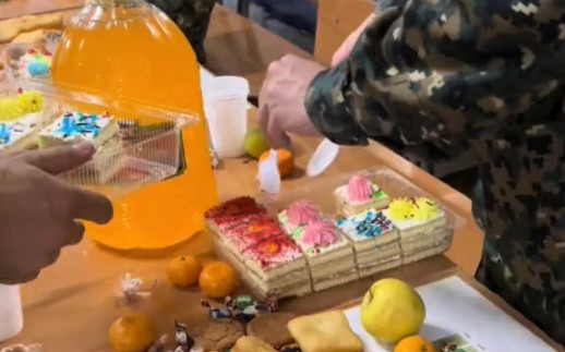 哈萨克斯坦陆军某部新年聚餐，可以看到桌上有各种果汁、奶油蛋糕、油炸食品、水果和糖果等