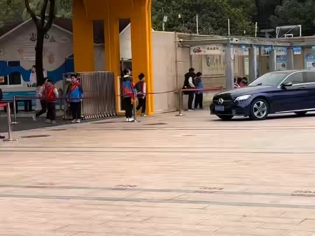 杭州某小学门口，学生站立校门口两侧夹道欢迎进入学校的机动车辆，并且学生们向这些机动车行少先队队礼，喊到："老师早"，"老师好"早祝语！